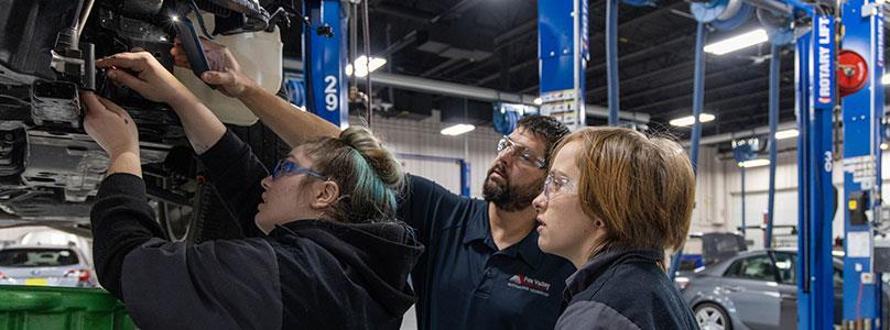 two students and an instructor working on a car