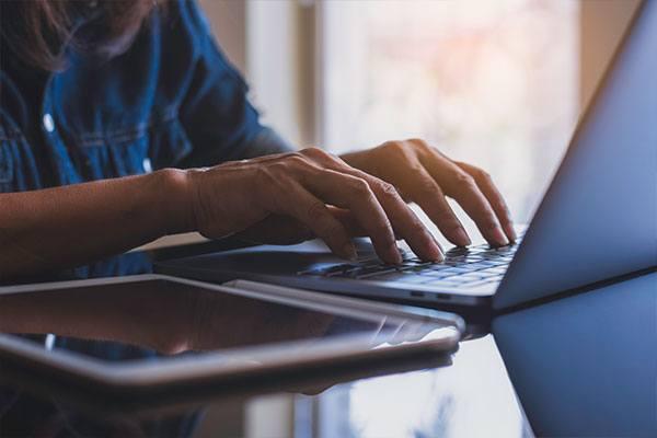 person typing on a keyboard looking toward a laptop and monitor