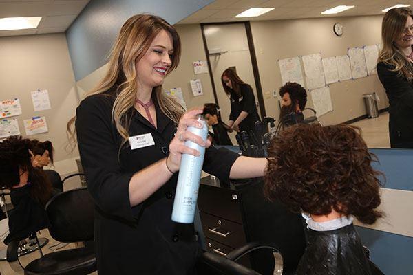 stylist spraying hairspray on hair of cosmetology mannequin head