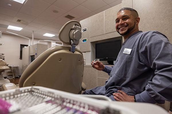 dental student with dental tool sitting next to dentist chair