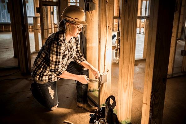 electrician wearing hard hat working with wires in electric outlet box on construction site