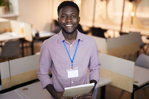 smiling man with lanyard holding notebook in office setting