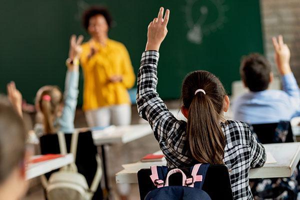 teacher in front of chalkboard with students in foreground raising their hands