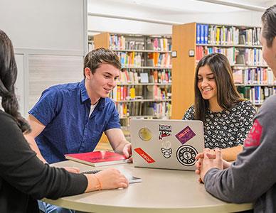 students around a laptop working on a project in the library