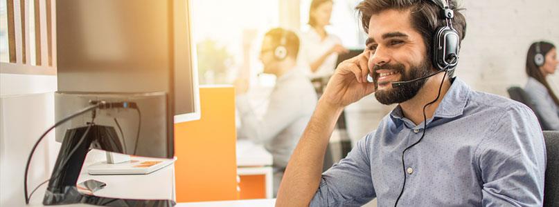 smiling man with headset sitting in office with other people in headsets in background